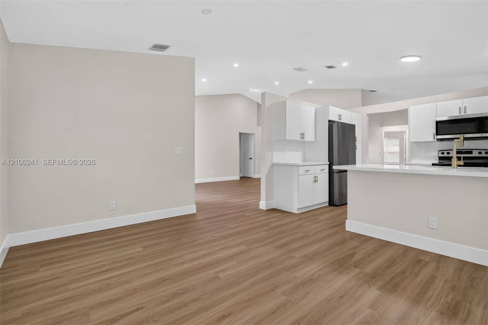 9407 SW 18th Street, Miramar, FL 33025 Interior featuring wood-finish flooring, vaulted ceilings, recessed lighting, white cabinetry, and a peninsula with a stone-surface countertop