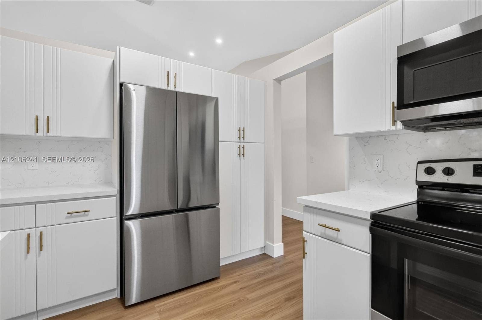 9407 SW 18th Street, Miramar, FL 33025 White shaker-style cabinetry with gold-tone hardware, stone-finish countertops, full-height stone backsplash, stainless steel French-door refrigerator, and wood-finish flooring