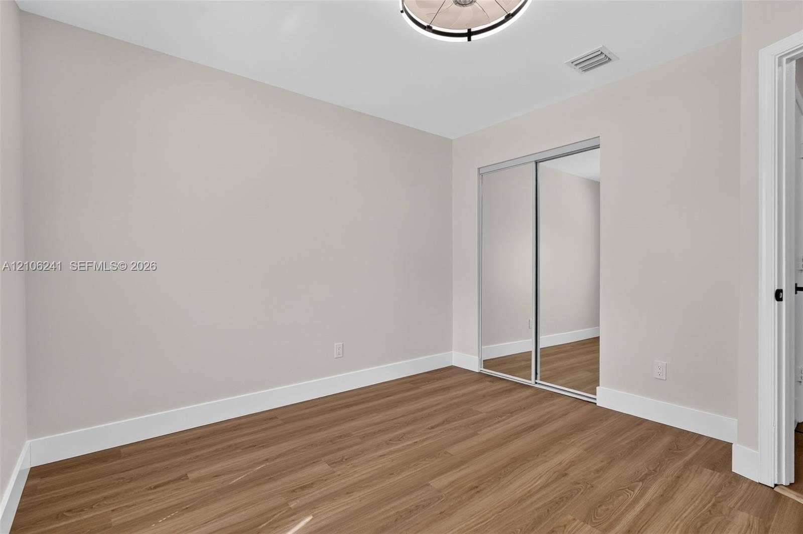 9407 SW 18th Street, Miramar, FL 33025 Room featuring wood-finish flooring, neutral wall paint, a ceiling-mounted light fixture, and a sliding-door mirrored closet