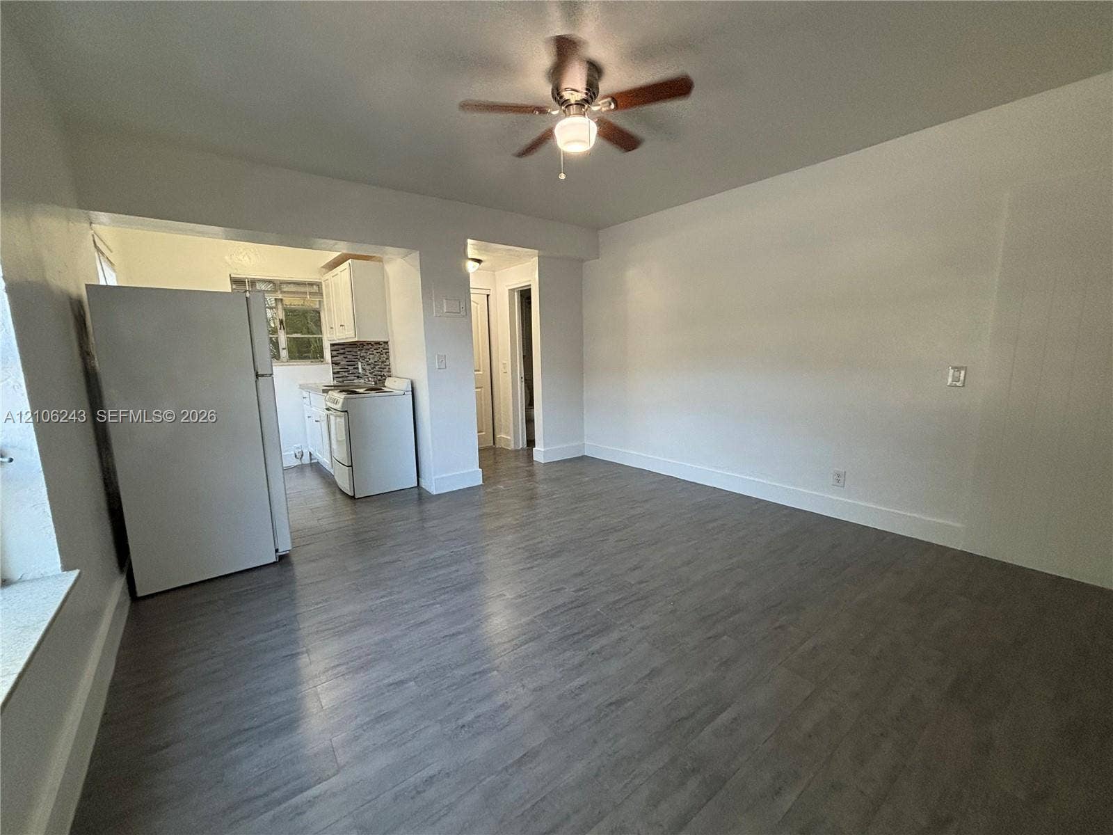 Open-concept area featuring wood-finish flooring, a ceiling fan with integrated lighting, and kitchen cabinetry paired with a decorative tile backsplash