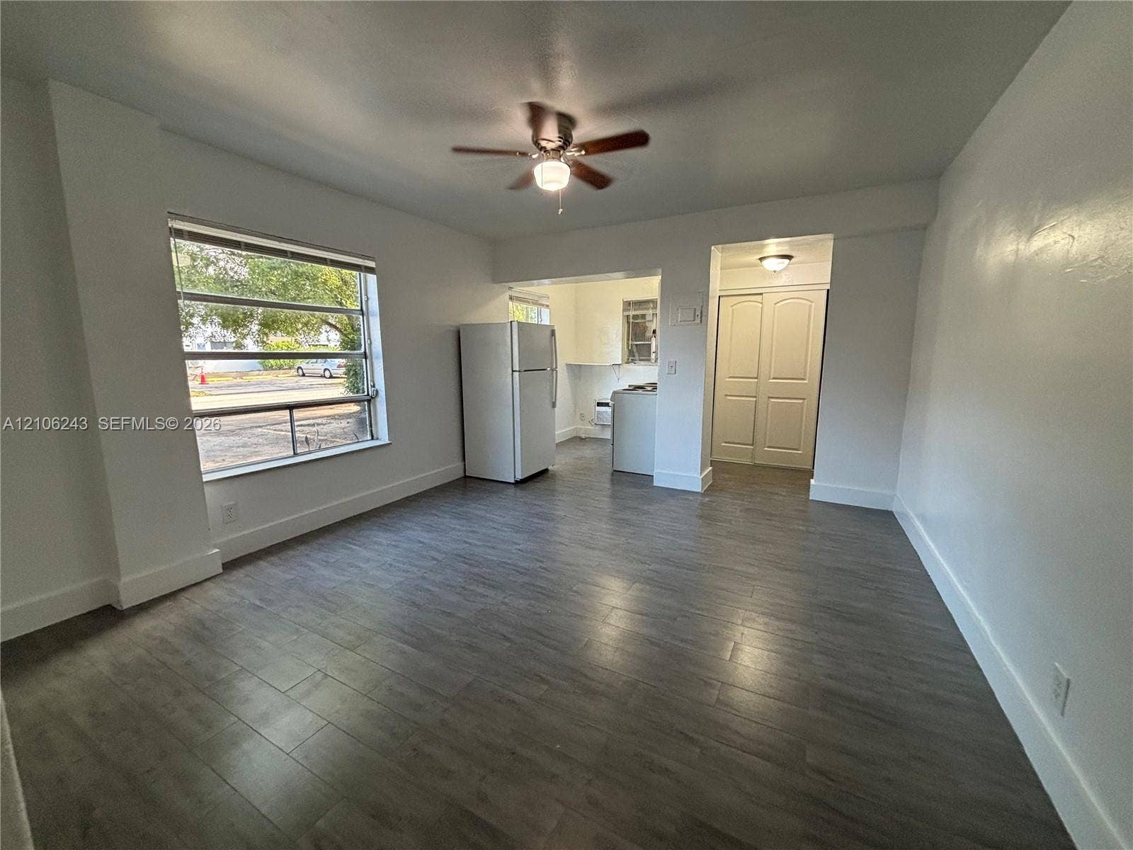 Living area featuring wood-finish flooring, a ceiling fan with integrated lighting, and large window