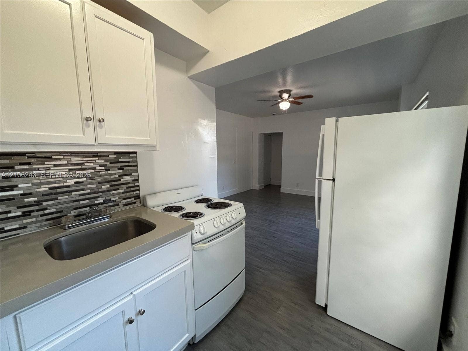 Kitchen featuring white cabinetry, solid-surface countertops, mosaic tile backsplash, stainless steel sink with a goose-neck faucet, and wood-finish flooring