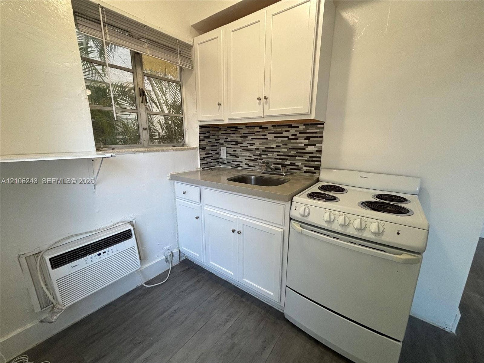 Kitchen featuring white cabinetry, solid-surface countertops, mosaic tile backsplash, stainless steel sink, and wood-finish flooring