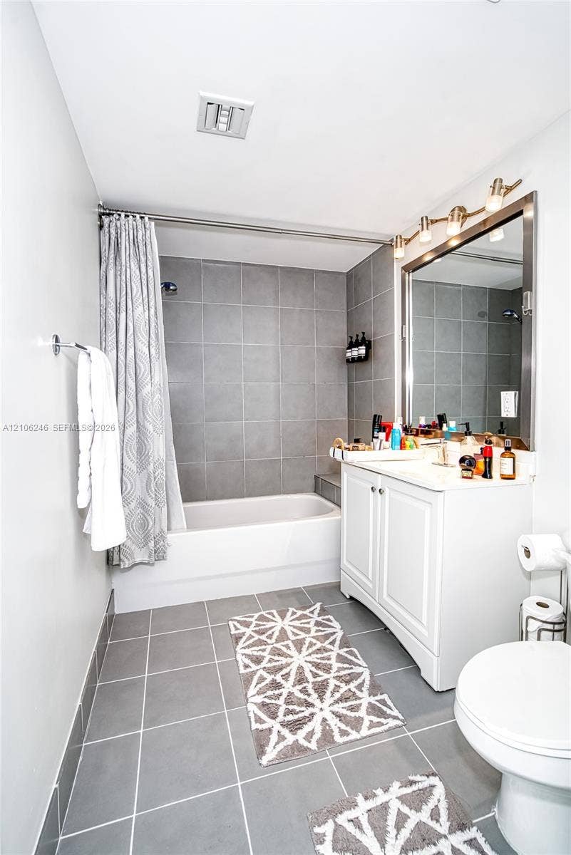 92 SW 3rd Street, #1511, Miami, Miami, FL 33130 Bathroom featuring a white vanity cabinet, a rectangular mirror with a metal frame, a multi-bulb vanity light fixture, and a bathtub with gray tile surround and flooring