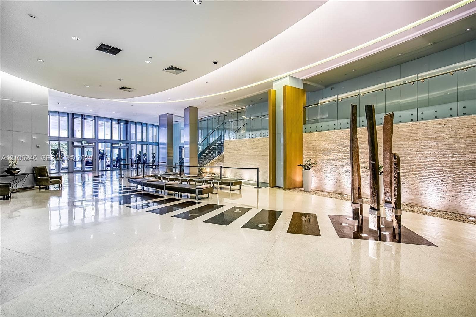 92 SW 3rd Street, #1511, Miami, Miami, FL 33130 Grand lobby featuring polished stone flooring, curved recessed ceiling lighting, full-height floor-to-ceiling windows, stacked-stone accent wall, and glass-paneled staircase railing