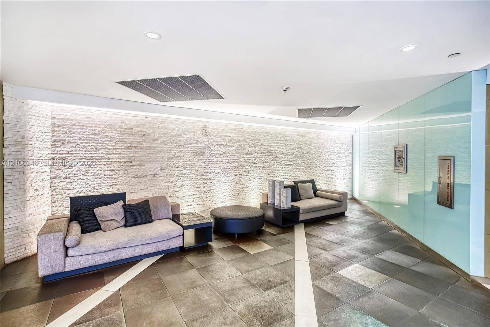 92 SW 3rd Street, #1511, Miami, Miami, FL 33130 Curved stone-textured accent wall with integrated LED uplighting, large-format tile flooring with contrasting linear inlays, and floor-to-ceiling glass paneling