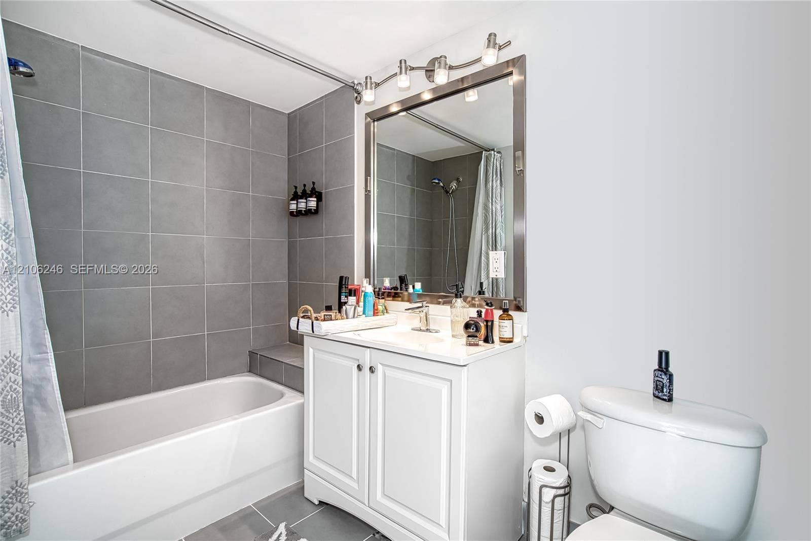 92 SW 3rd Street, #1511, Miami, Miami, FL 33130 Bathroom featuring a white vanity with built-in cabinetry, a rectangular basin with a single-handle faucet, a framed mirror, a multi-bulb vanity light fixture, and a tiled bathtub surround