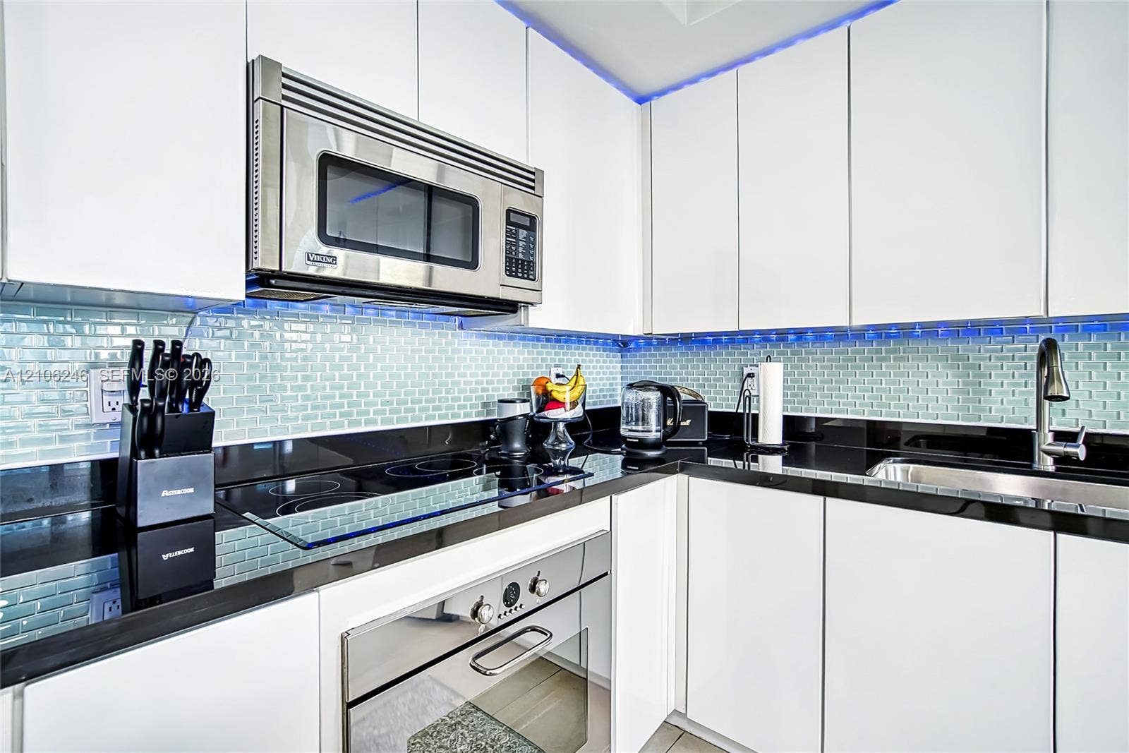 92 SW 3rd Street, #1511, Miami, Miami, FL 33130 Modern kitchen featuring flat-panel white cabinetry, contrasting black countertops, glass subway tile backsplash, stainless steel built-in microwave, and stainless steel oven
