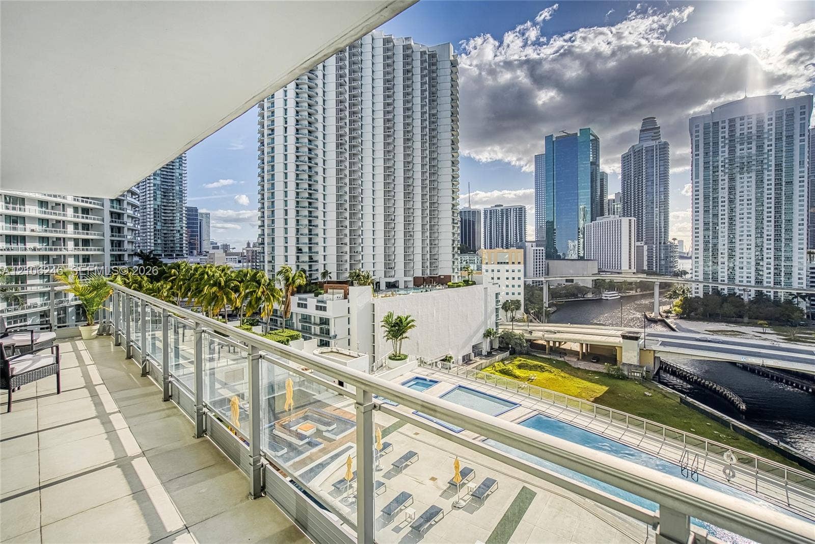 92 SW 3rd Street, #1511, Miami, Miami, FL 33130 Covered balcony featuring tile flooring and a glass-paneled railing overlooking an urban skyline and multi-level swimming pools