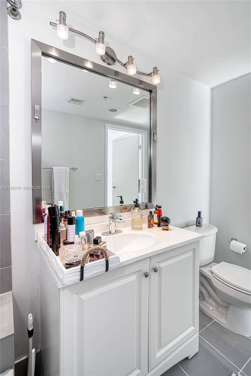 92 SW 3rd Street, #1511, Miami, Miami, FL 33130 White vanity featuring a smooth countertop with an integrated basin, polished metal hardware, a large framed mirror, and four-light vanity fixture