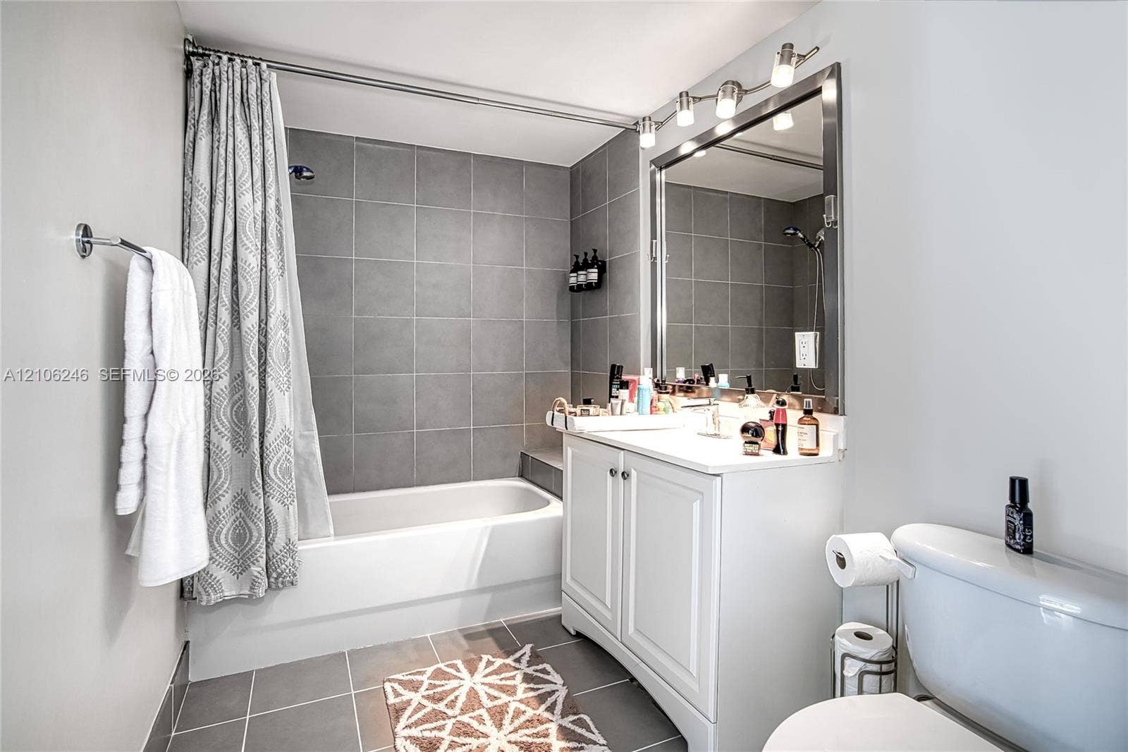 92 SW 3rd Street, #1511, Miami, Miami, FL 33130 Bathroom featuring a white vanity cabinet with a solid surface countertop, an expansive framed vanity mirror, multi-bulb overhead lighting, and a shower-tub combination with grey tile surround and large-format floor tiling