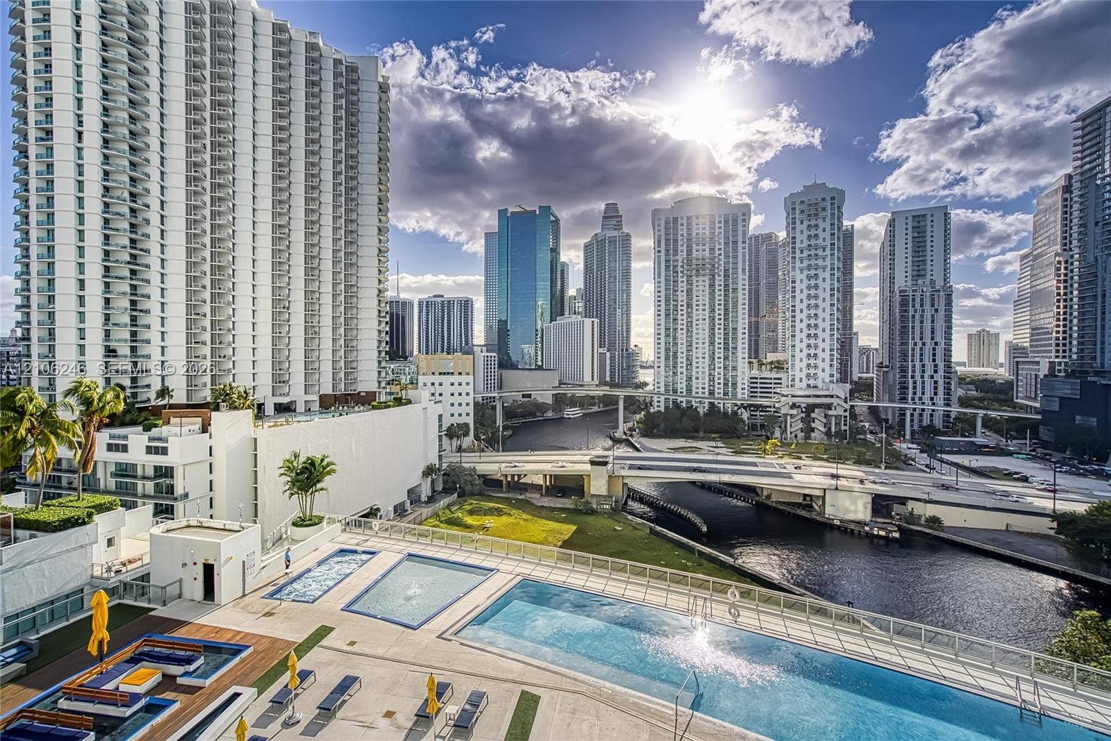 92 SW 3rd Street, #1511, Miami, Miami, FL 33130 Outdoor pool terrace featuring tiered swimming areas, sun deck with stone-finish tiling, glass panel perimeter railing, and urban skyline backdrop