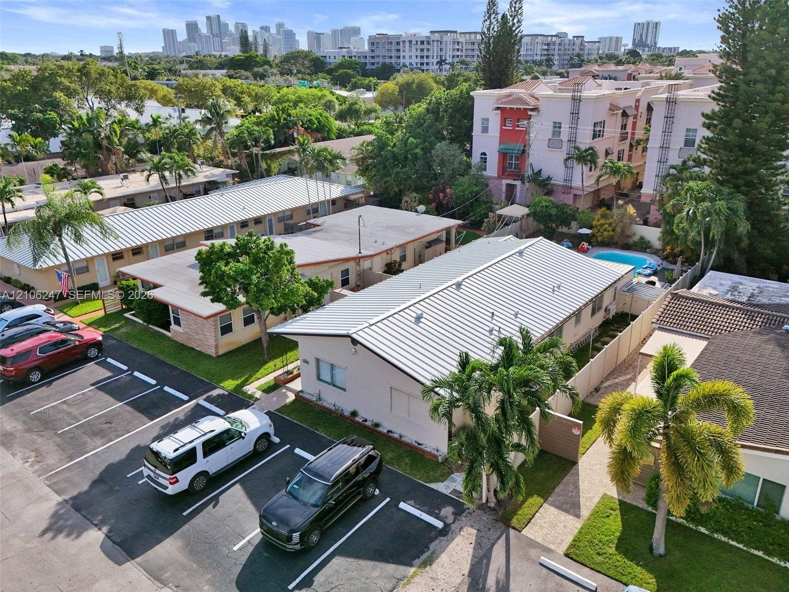 1037 N Victoria Park Road, #2, Fort Lauderdale, Fort Lauderdale, FL 33304 Aerial perspective of the property featuring light-toned exterior siding, metal roofing, designated asphalt parking spaces, and mature palm landscaping