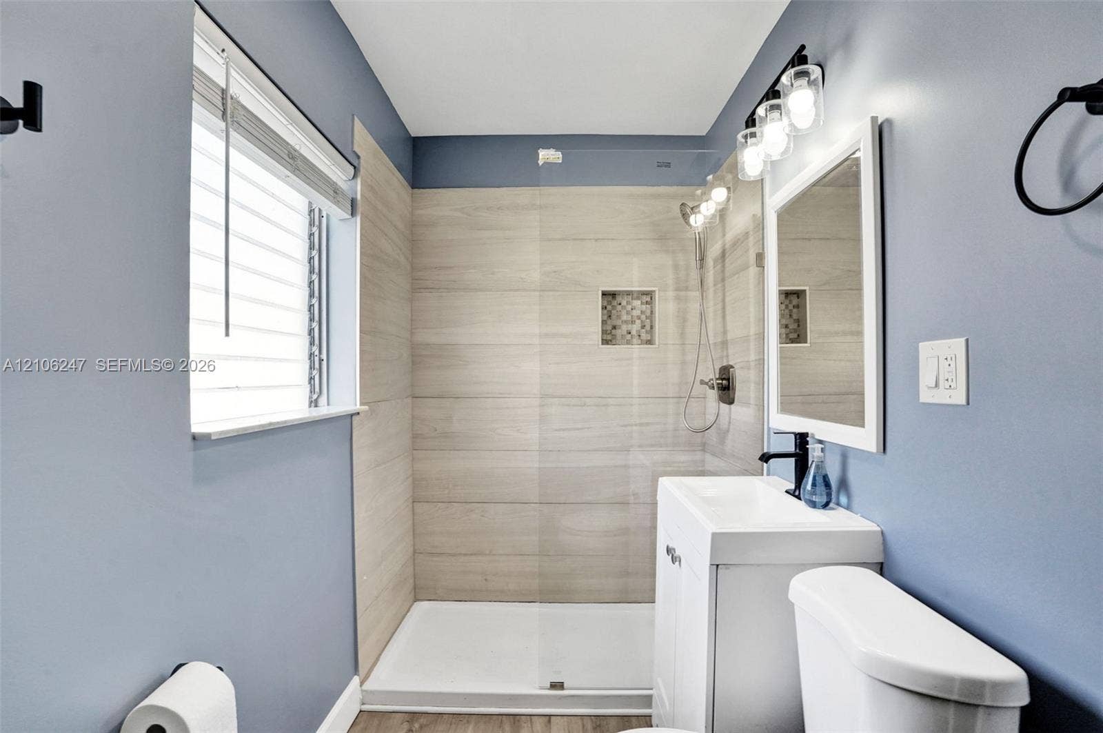 1037 N Victoria Park Road, #2, Fort Lauderdale, Fort Lauderdale, FL 33304 Bathroom featuring a walk-in shower with horizontal tile surround and inset niche, a pedestal sink with matte black faucet, a framed mirror, and three-bulb vanity lighting
