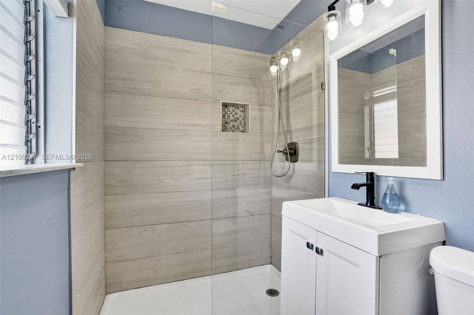 1037 N Victoria Park Road, #2, Fort Lauderdale, Fort Lauderdale, FL 33304 Walk-in shower featuring wood-finish tile surround, integrated mosaic tile niche, frameless glass panel, and handheld shower fixture