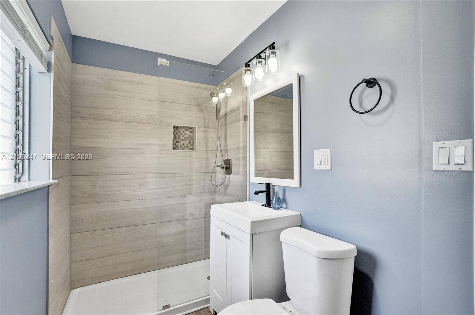 1037 N Victoria Park Road, #2, Fort Lauderdale, Fort Lauderdale, FL 33304 Walk-in shower with horizontal tile surround, glass panel door, built-in shower niche, white vanity cabinet with a rectangular sink, and three-light wall-mounted vanity fixture