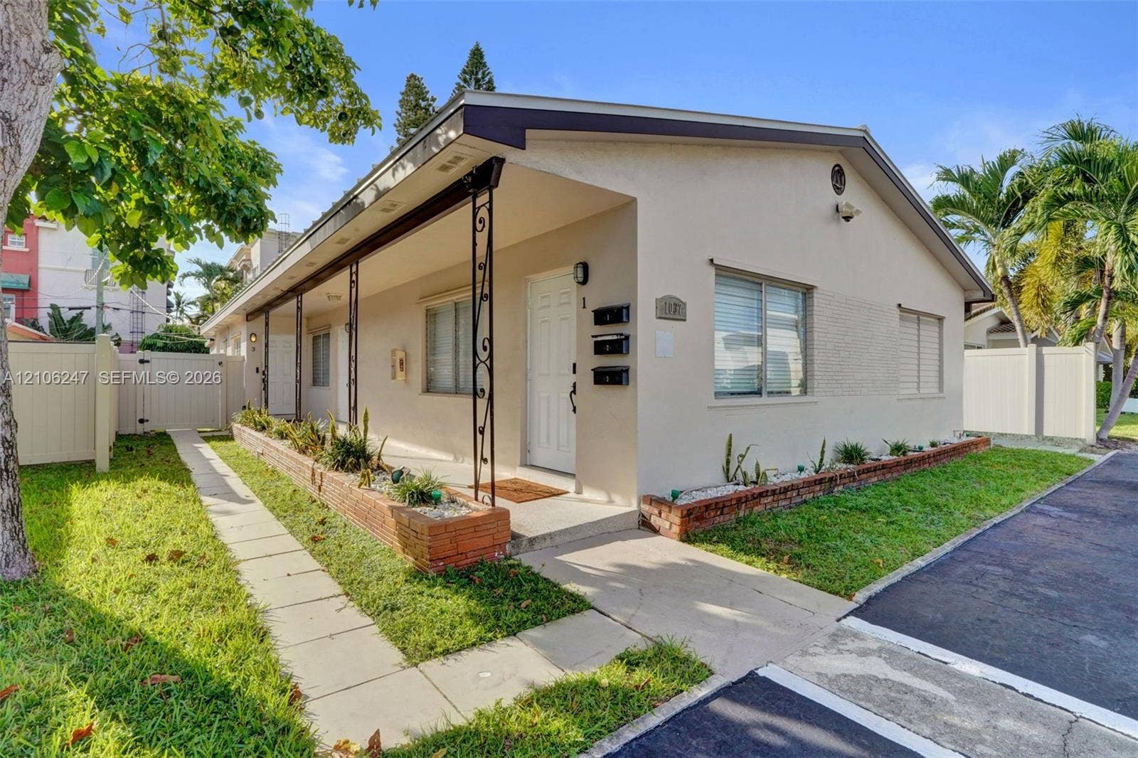1037 N Victoria Park Road, #2, Fort Lauderdale, Fort Lauderdale, FL 33304 Single-story exterior featuring a covered porch with ornamental metal supports, brick-trimmed landscaping beds, and a white privacy fence