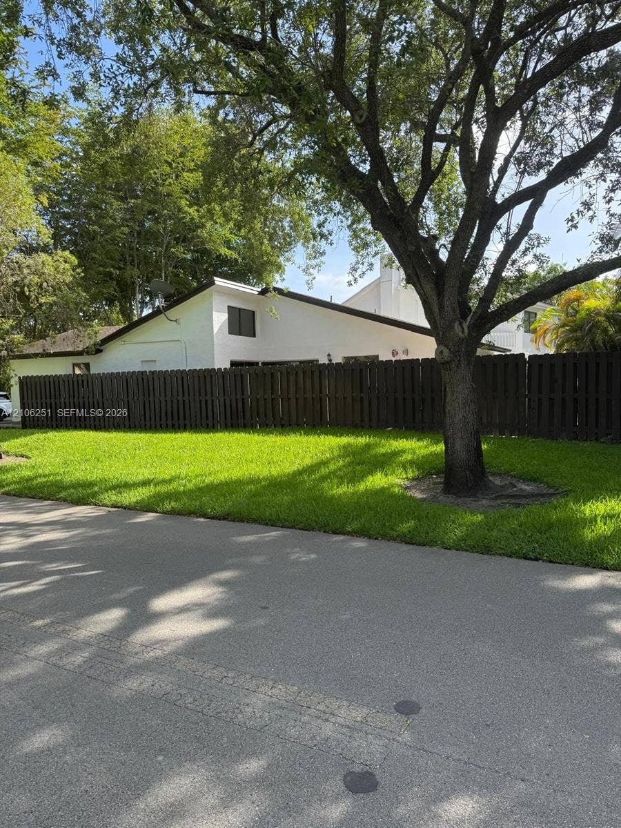 Exterior featuring a white stucco facade, a dark-toned vertical wood privacy fence, and a mature landscape with established trees
