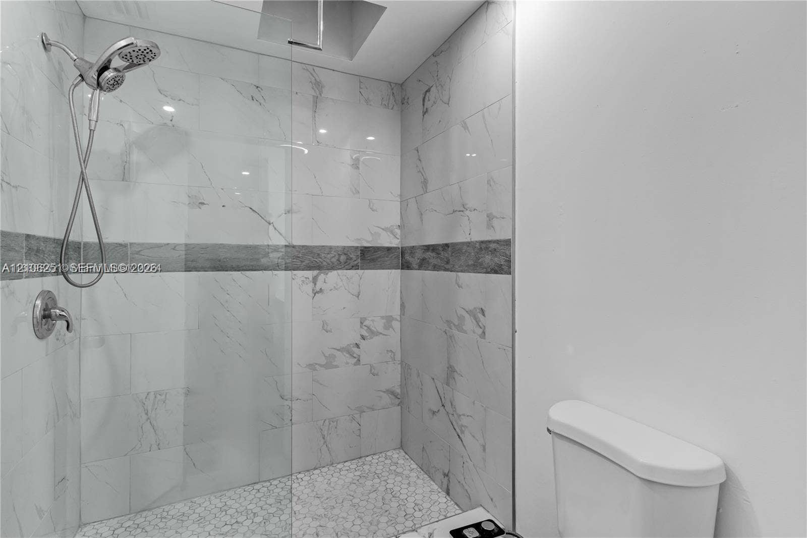 Walk-in shower featuring floor-to-ceiling stone-finish wall tile, a horizontal decorative accent border, pebble-style floor tiling, a frameless glass enclosure, and a multi-function shower head