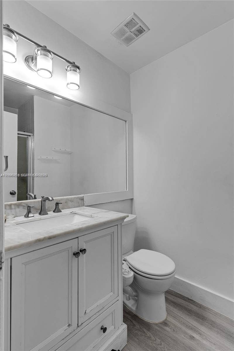 Bathroom featuring a wood-finish vanity with a stone-top integrated sink, a large wall-mounted mirror, a three-light fixture, and wood-finish flooring