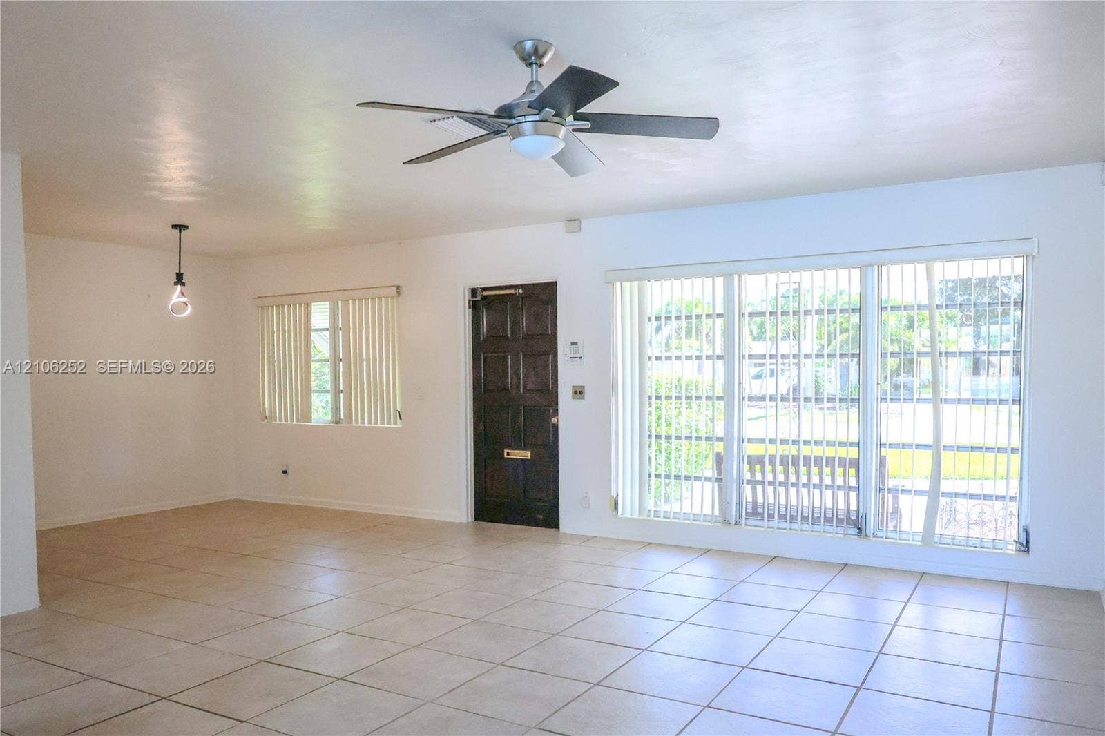 225 E Ilex Drive, Lake Park, Lake Park, FL 33403 Living area featuring large-format ceramic tile flooring, a multi-blade ceiling fan with integrated light, a paneled wood entry door, and expansive floor-to-ceiling windows