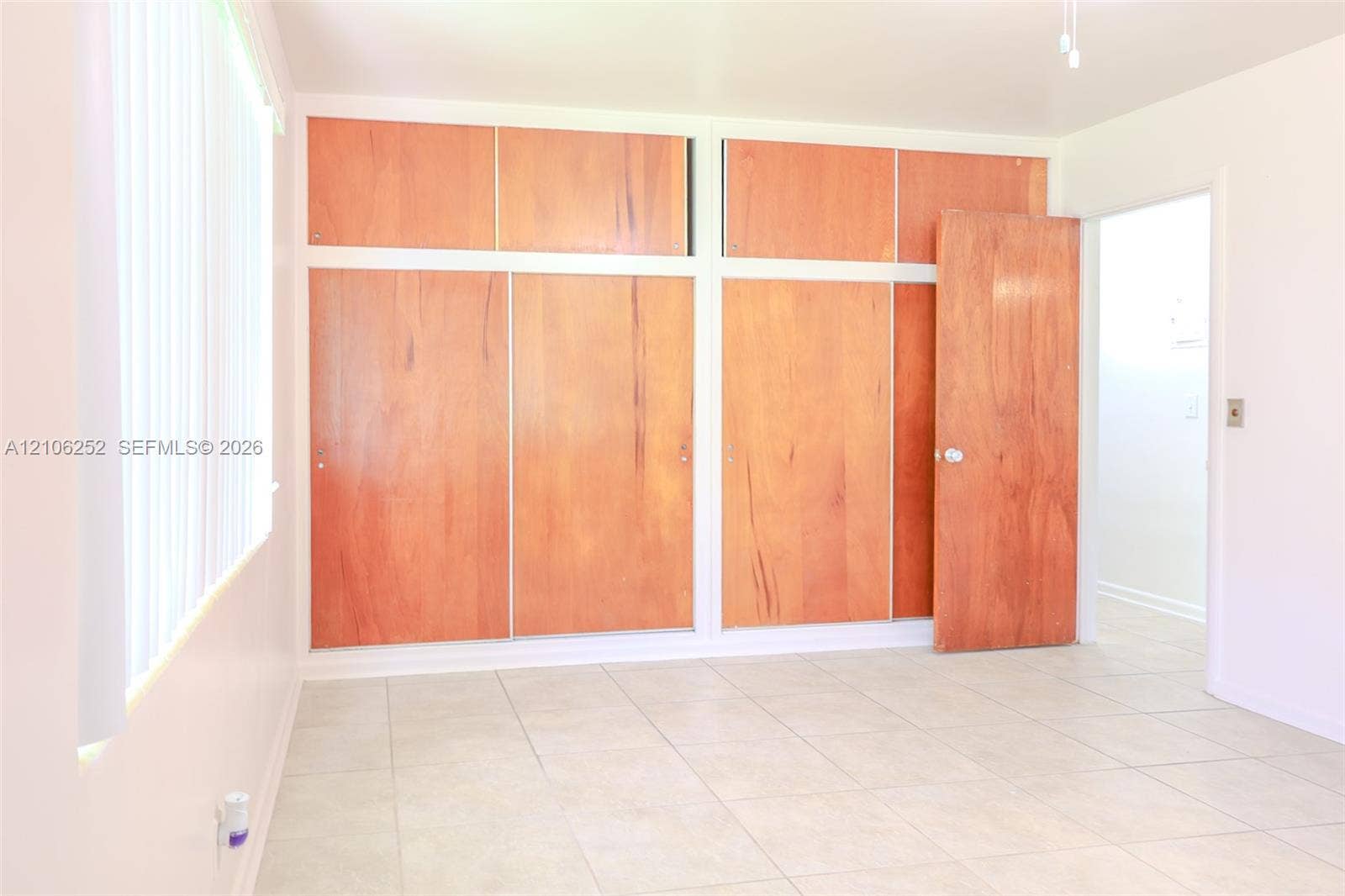 225 E Ilex Drive, Lake Park, Lake Park, FL 33403 Wall-to-wall built-in wood-finish cabinetry with overhead storage, neutral tile flooring, and vertical blinds
