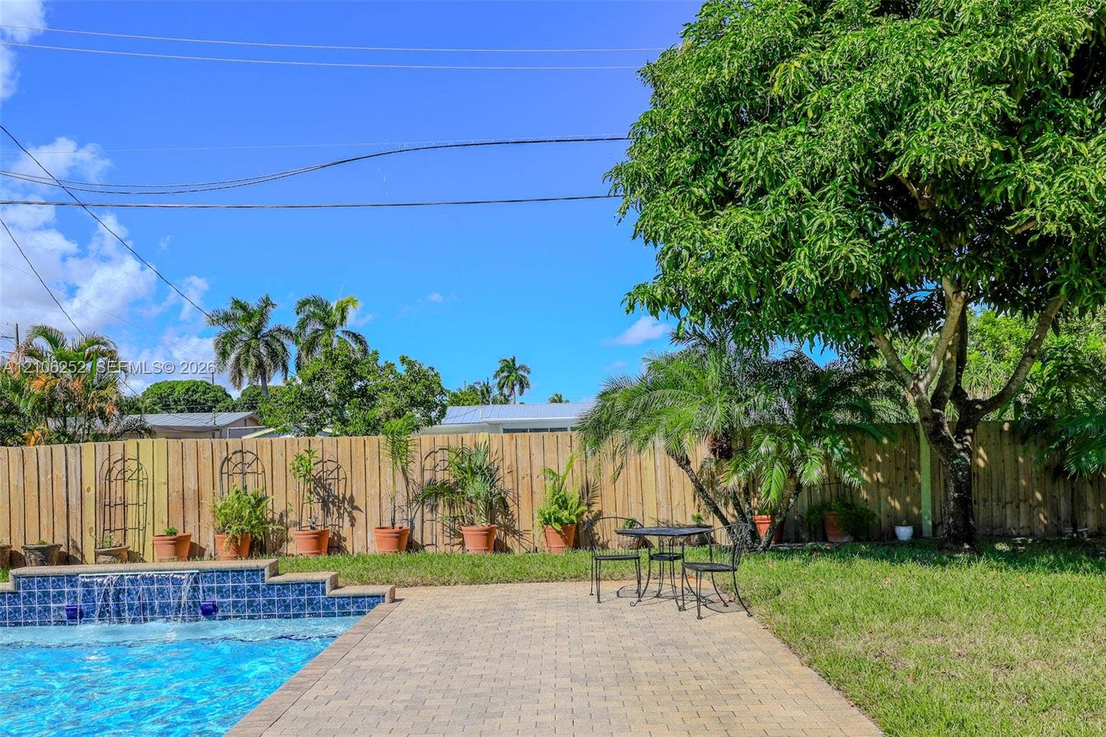 225 E Ilex Drive, Lake Park, Lake Park, FL 33403 Backyard featuring a swimming pool with a stone-finish spillway, concrete paver patio, wood-panel fencing, and mature trees