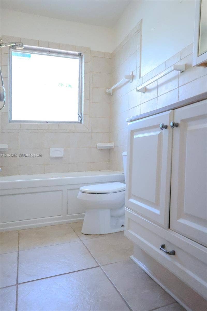 225 E Ilex Drive, Lake Park, Lake Park, FL 33403 Bathroom featuring white cabinetry, tile flooring, wall-mounted towel bars, and a built-in tub with tile surround