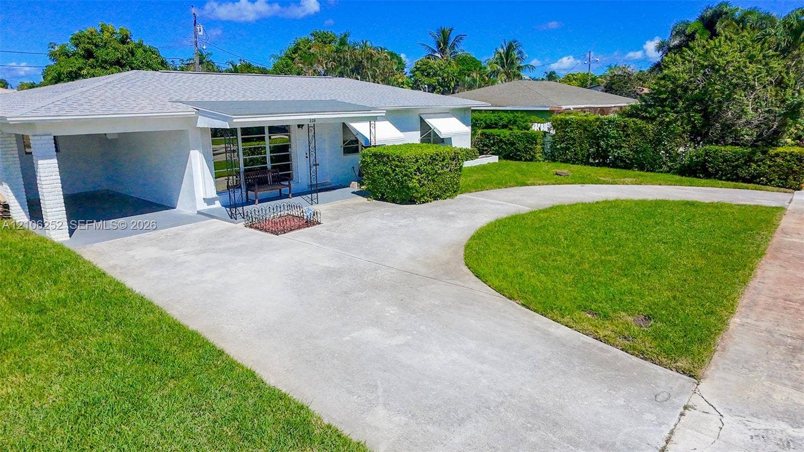 225 E Ilex Drive, Lake Park, Lake Park, FL 33403 Single-story residence featuring a painted masonry exterior, covered carport, metal-framed window awnings, and a concrete driveway