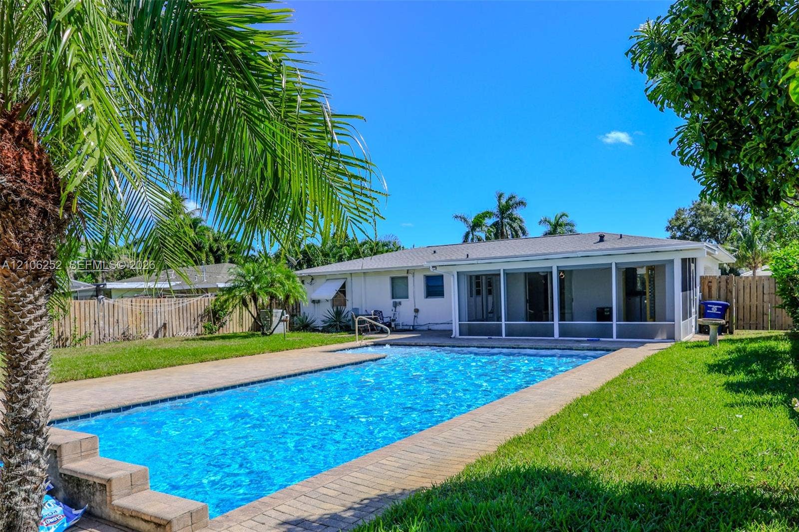 225 E Ilex Drive, Lake Park, Lake Park, FL 33403 Private backyard featuring a rectangular swimming pool, paver patio surround, screen-enclosed porch, and wood privacy fencing