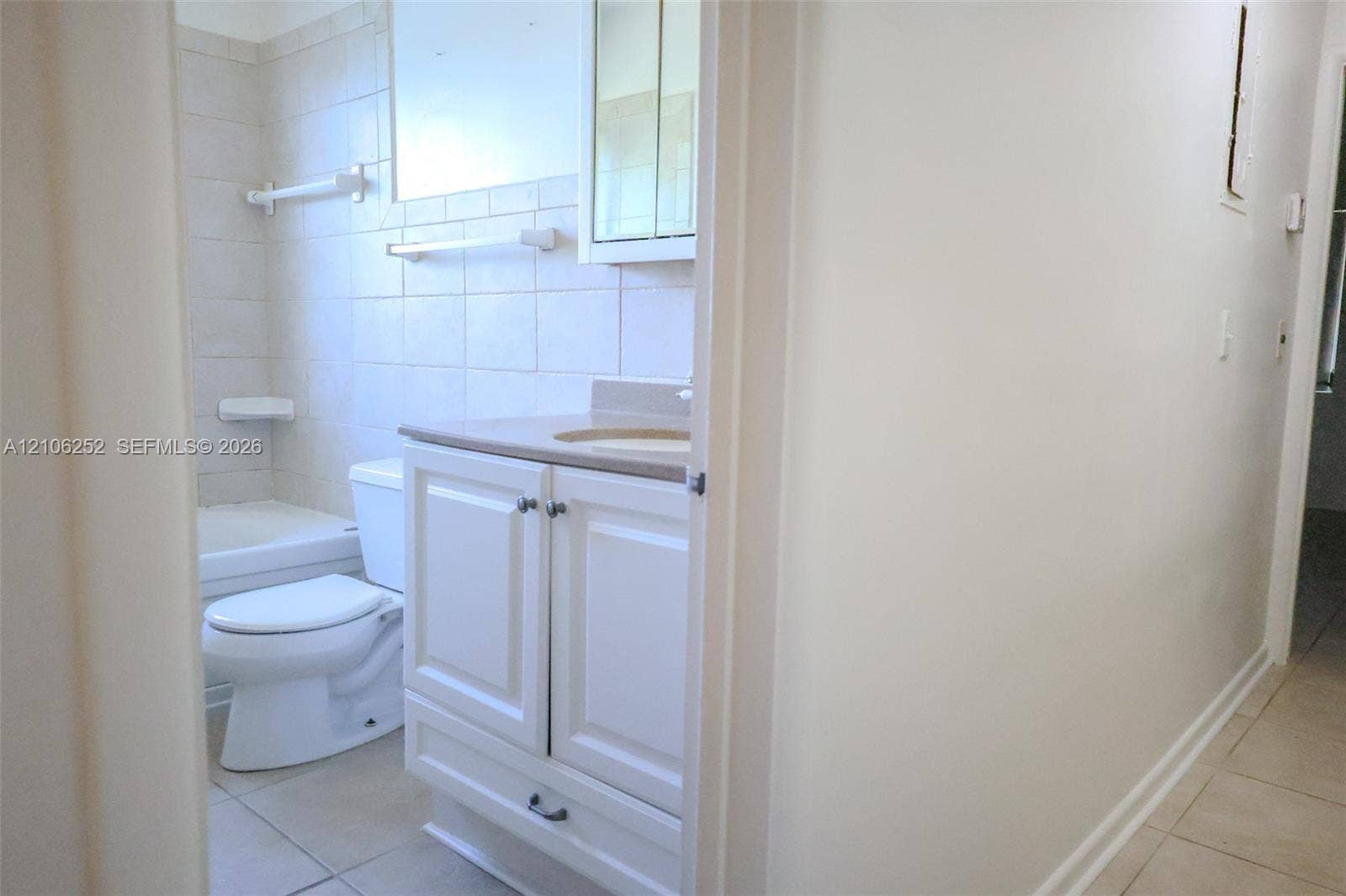 225 E Ilex Drive, Lake Park, Lake Park, FL 33403 Bathroom featuring a white vanity cabinet with an integrated countertop and sink, a mirrored medicine cabinet, a standard toilet, and a tiled tub surround