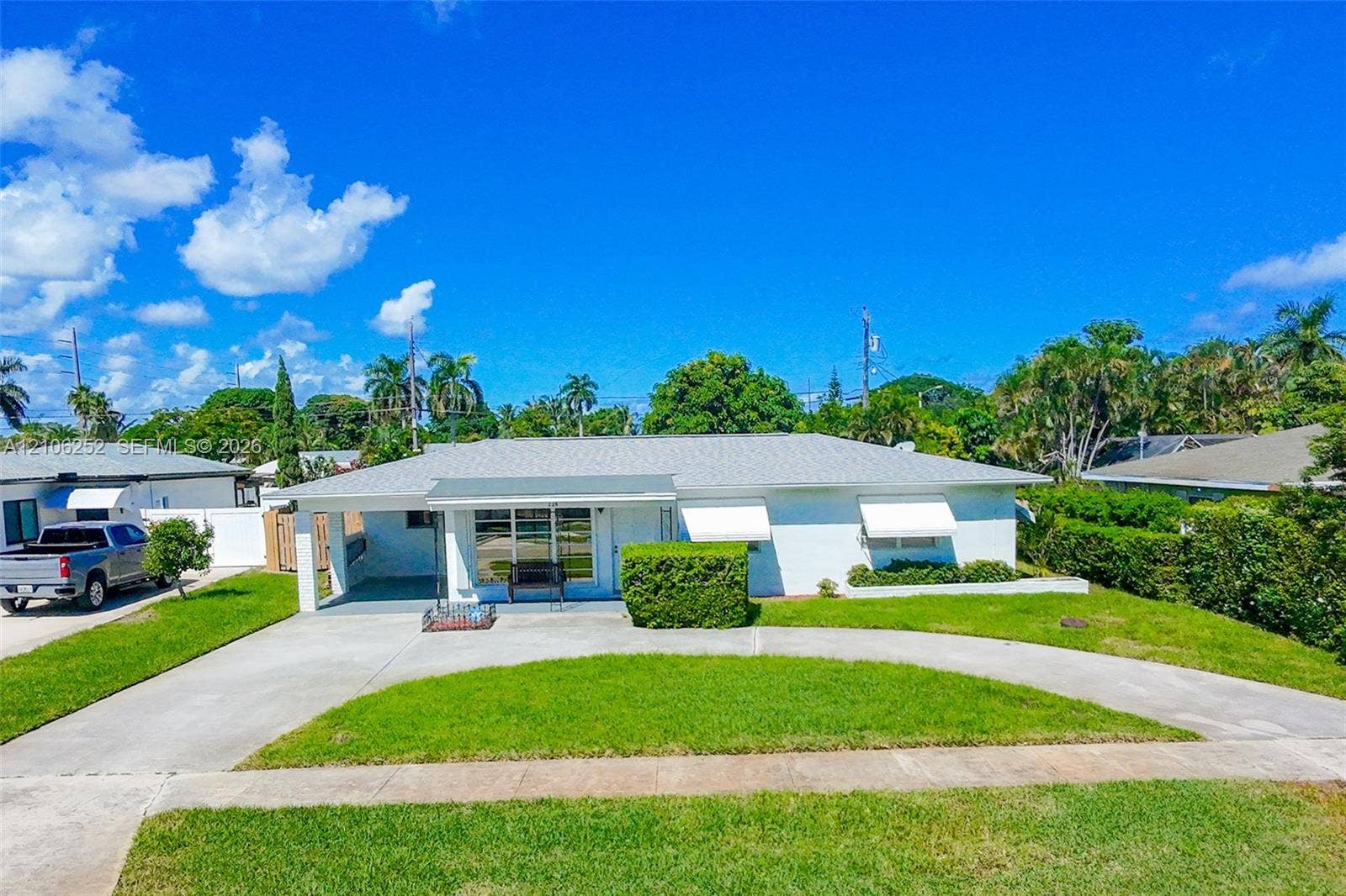 225 E Ilex Drive, Lake Park, Lake Park, FL 33403 Single-story residence featuring a painted masonry exterior, a covered carport, and retractable window awnings, set on a lot with a curved concrete driveway and lawn
