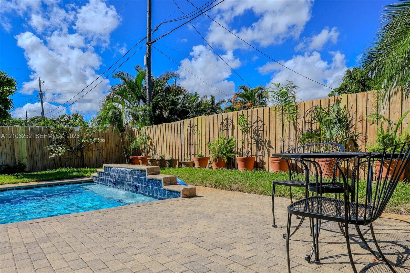 225 E Ilex Drive, Lake Park, Lake Park, FL 33403 Backyard featuring an in-ground swimming pool with a tiered tile waterfall, stone paver decking, and a wood privacy fence