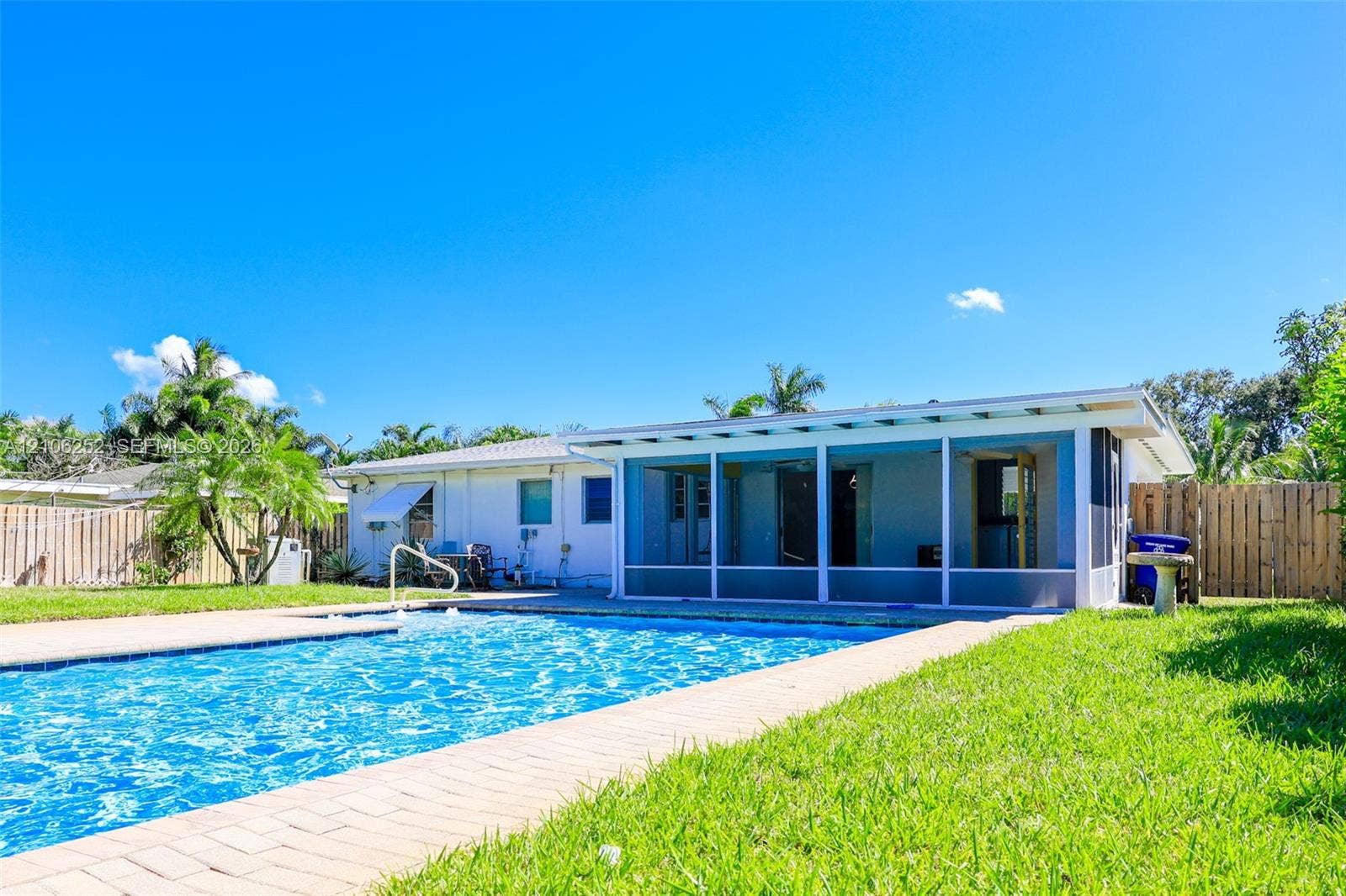 225 E Ilex Drive, Lake Park, Lake Park, FL 33403 Rear exterior featuring an in-ground swimming pool, brick paver decking, a screened-in lanai, and wood-style privacy fencing