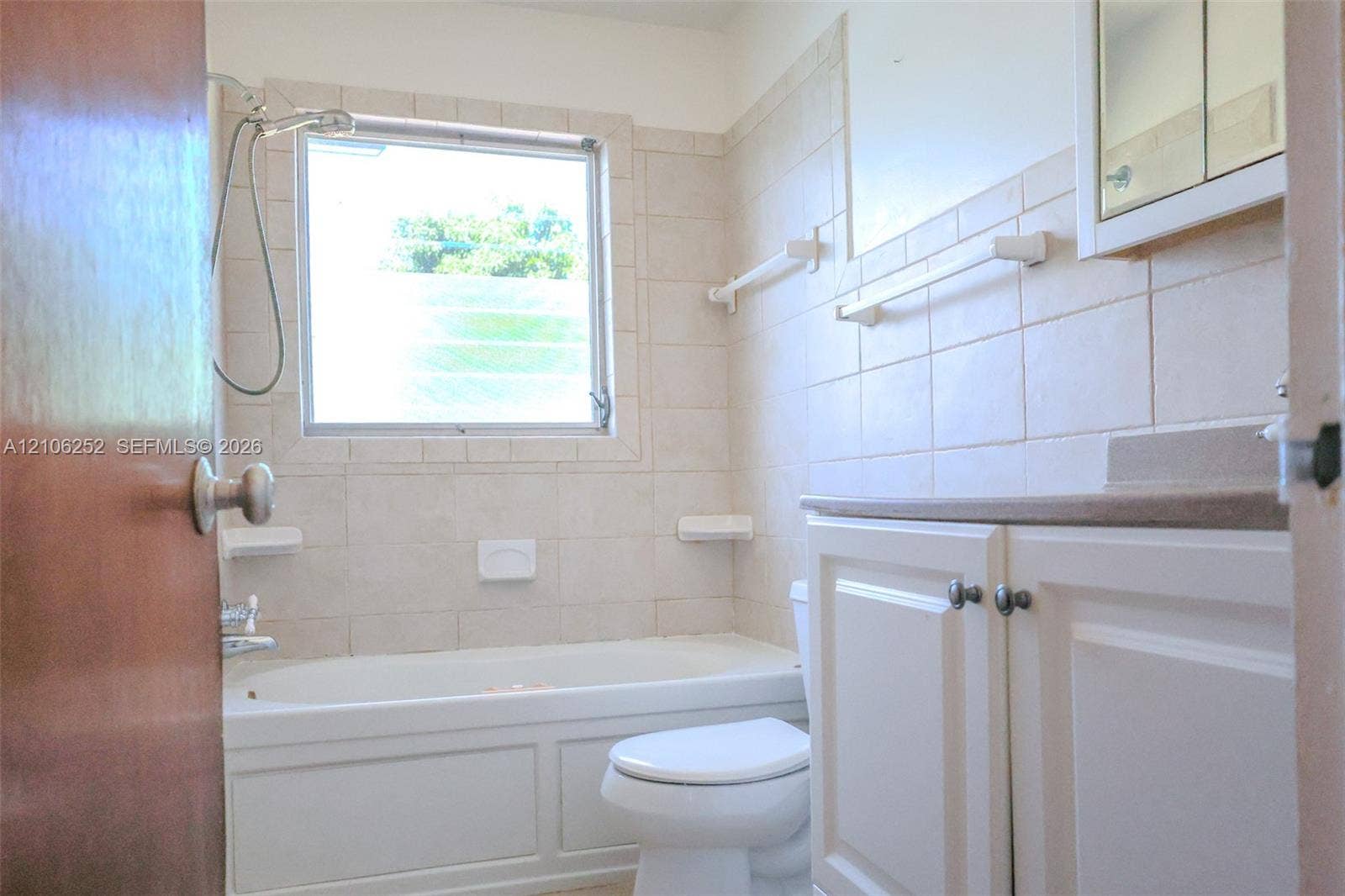 225 E Ilex Drive, Lake Park, Lake Park, FL 33403 Bathroom featuring a tub with a handheld shower fixture, light-toned wall tiling, a vanity with a countertop, and a recessed medicine cabinet
