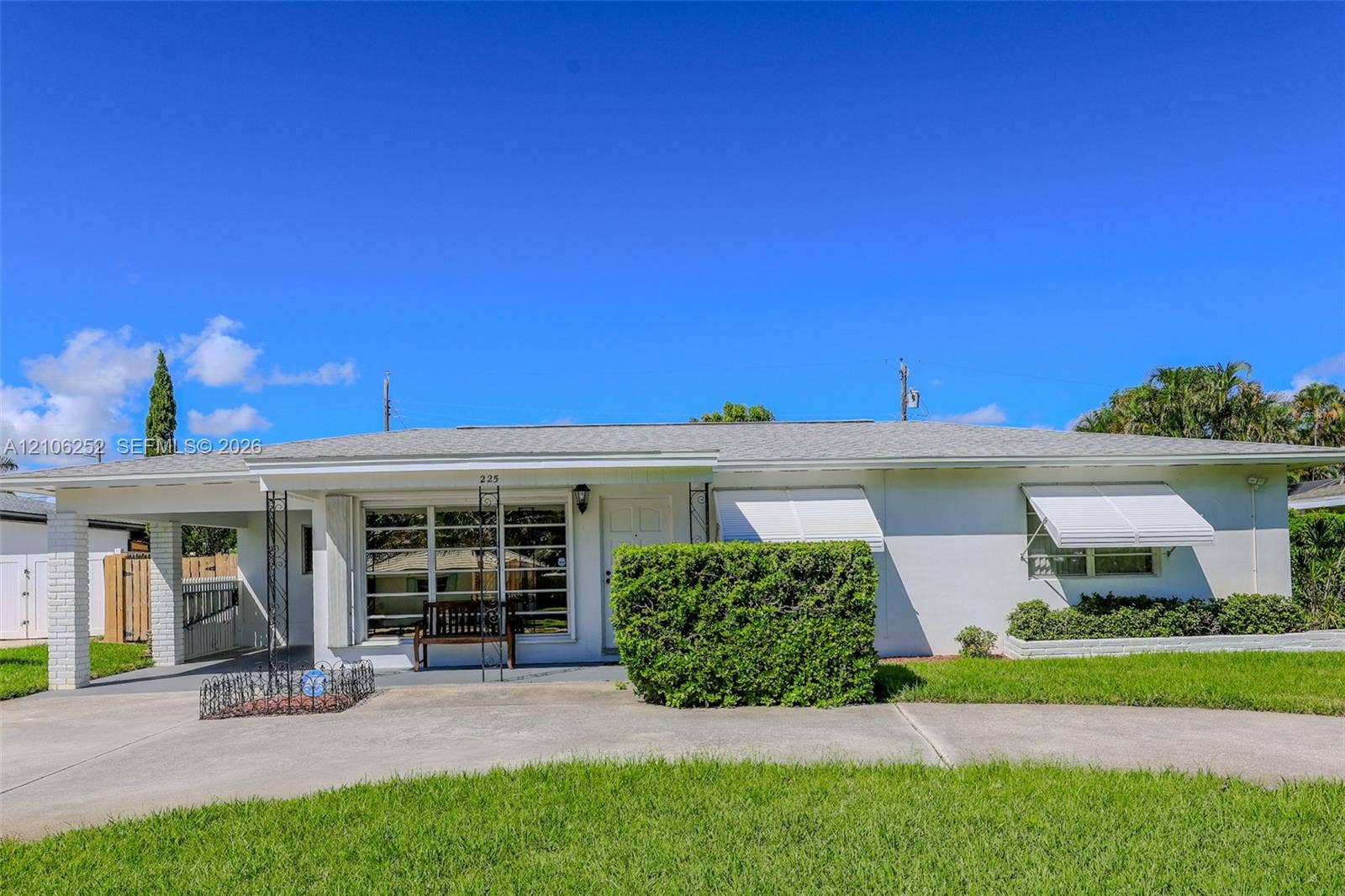 225 E Ilex Drive, Lake Park, Lake Park, FL 33403 Single-story residence featuring a painted masonry exterior, covered carport with decorative metal supports, multi-pane picture window, and retractable metal window awnings