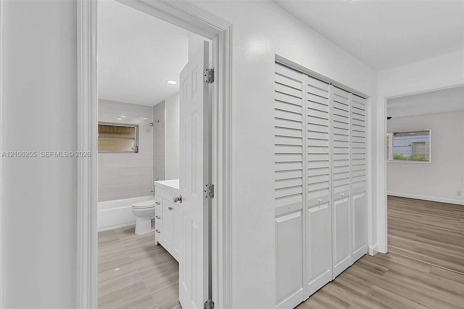 6118 Dusenburg Road, Delray Beach, FL 33484 Hallway featuring louvered closet doors, wood-finish flooring, and a bathroom entry with a white vanity and tiled shower enclosure