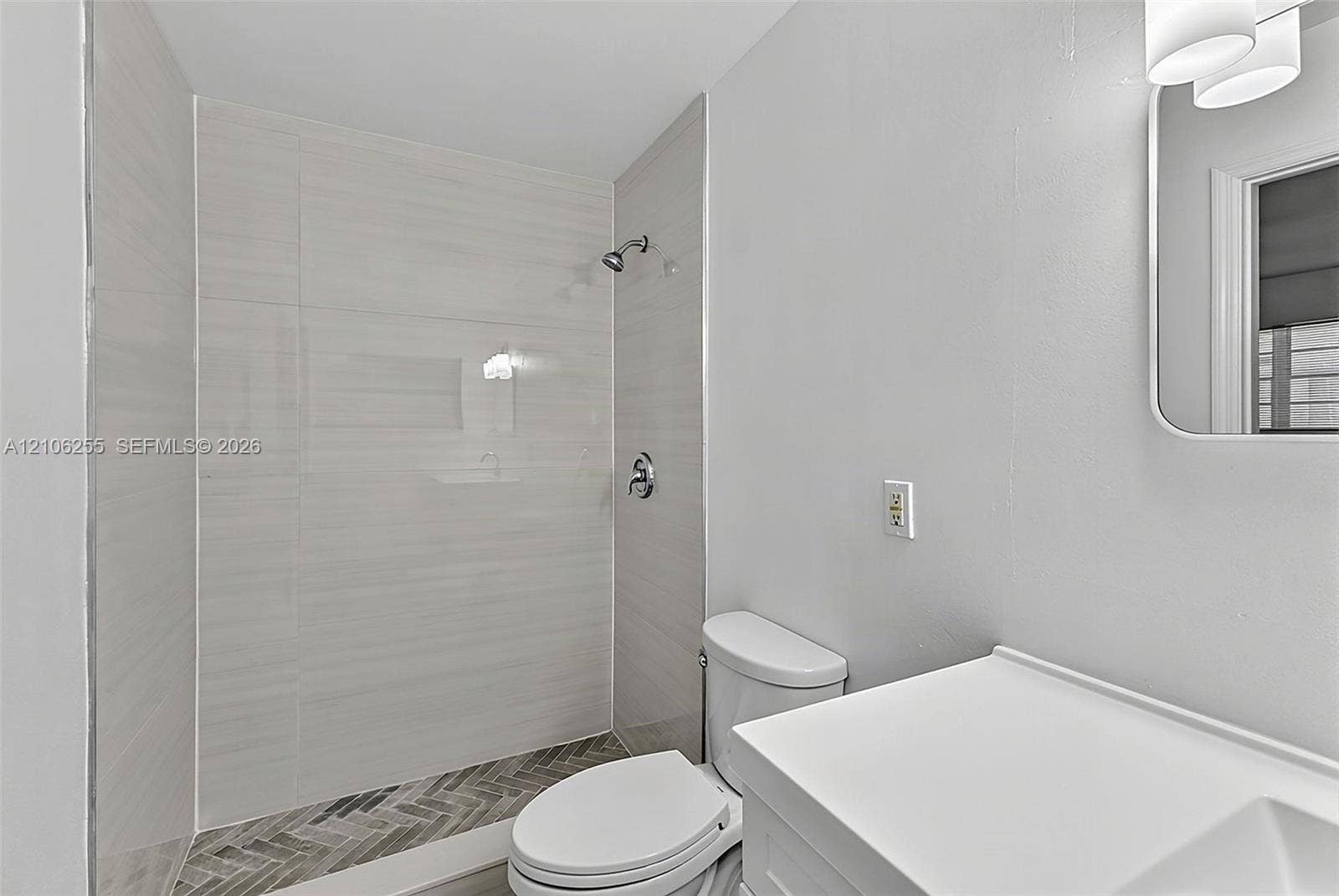 6118 Dusenburg Road, Delray Beach, FL 33484 Bathroom featuring a walk-in shower with large-format wall tile, herringbone-patterned floor tile, a white vanity, and a wall-mounted mirror