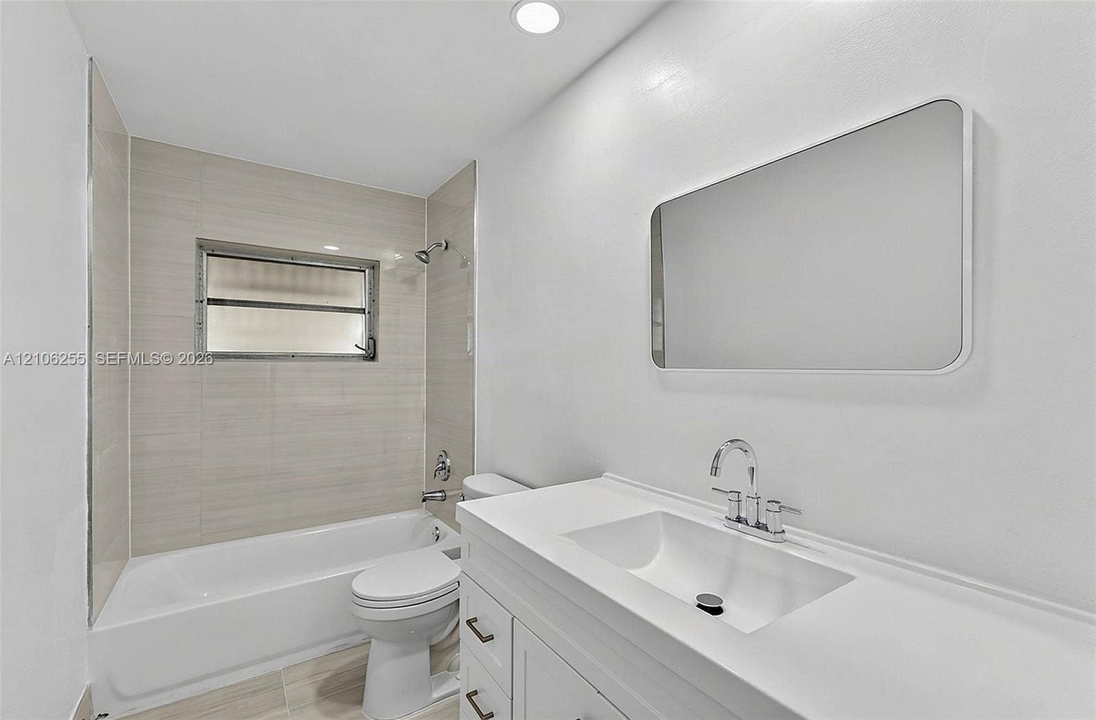 6118 Dusenburg Road, Delray Beach, FL 33484 Bathroom featuring a white vanity with an integrated sink, rectangular mirror, recessed lighting, and a bathtub with neutral tile surround