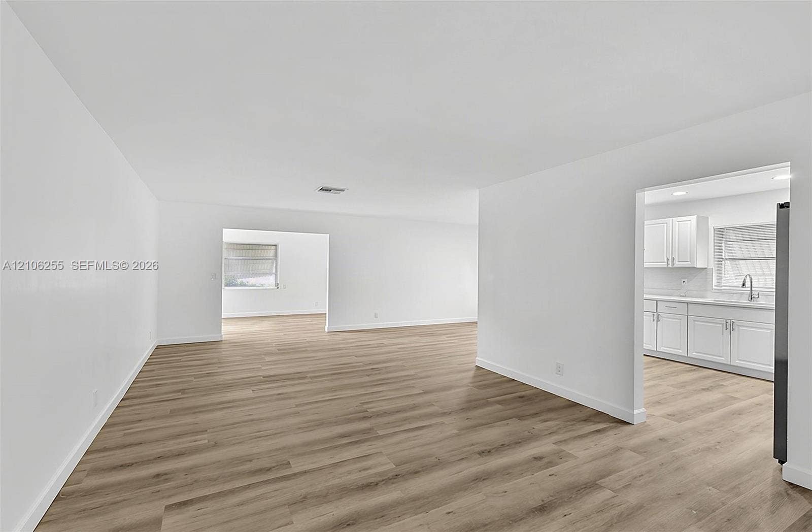 6118 Dusenburg Road, Delray Beach, FL 33484 Open interior space featuring wood-finish flooring, white walls, and a kitchen area with white cabinetry and a stainless steel faucet