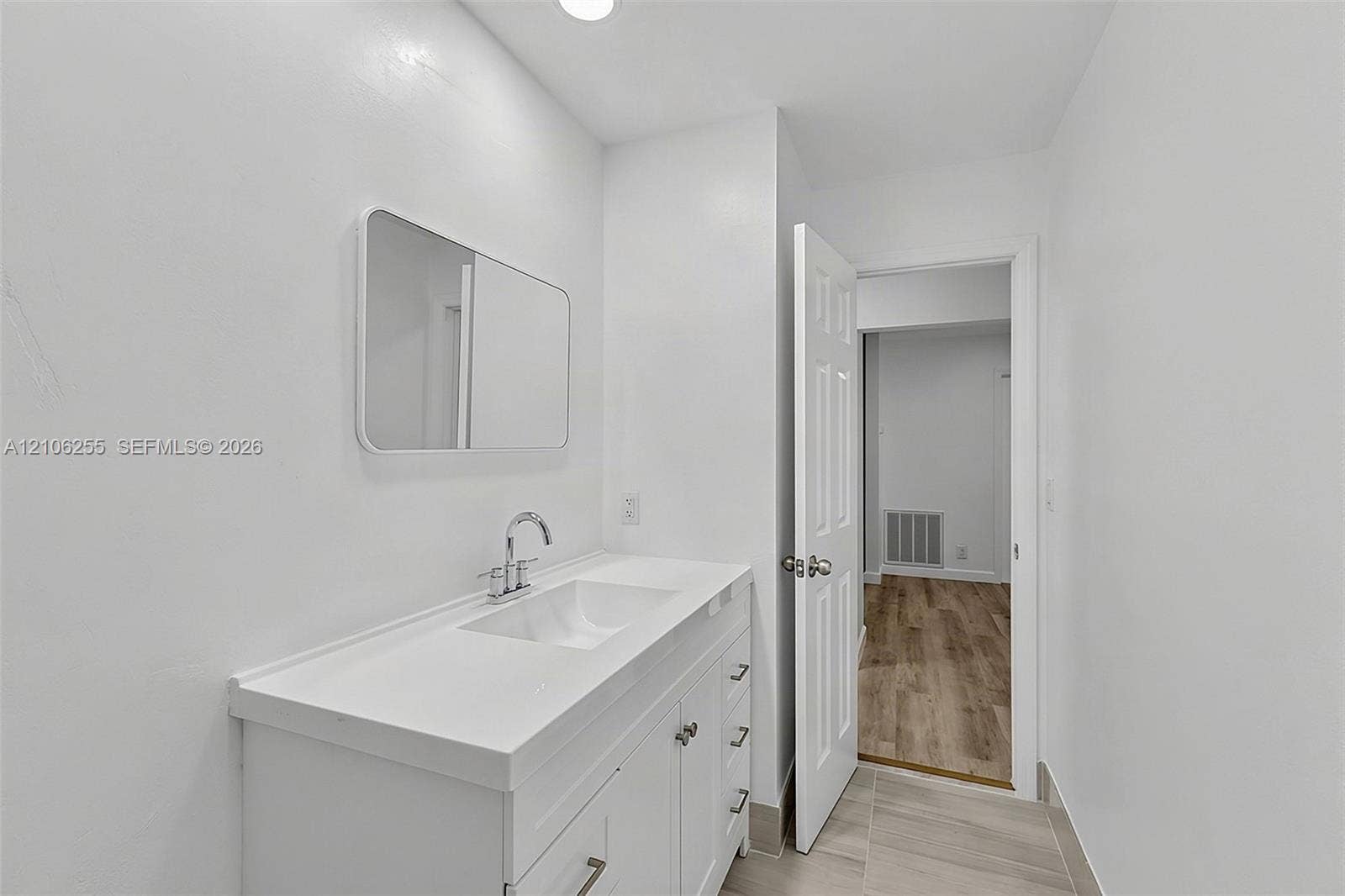 6118 Dusenburg Road, Delray Beach, FL 33484 Bathroom vanity with a white composite countertop, integrated rectangular sink, brushed chrome faucet, and rectangular wall-mounted mirror, featuring wood-finish flooring in the surrounding area