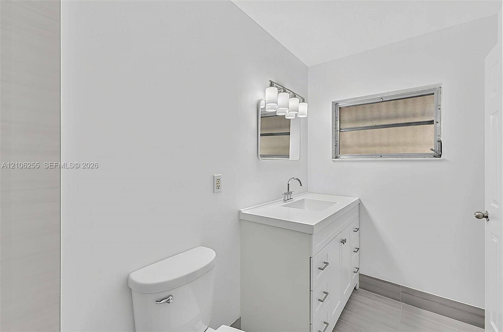 6118 Dusenburg Road, Delray Beach, FL 33484 White vanity with integrated basin, multi-drawer storage, polished metal faucet, multi-bulb vanity light, and gray tile flooring