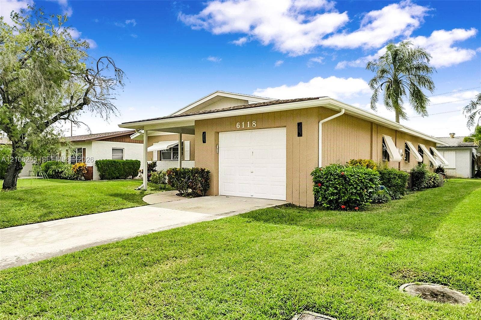 6118 Dusenburg Road, Delray Beach, FL 33484 Single-story exterior featuring a concrete driveway, attached garage, and metal window awnings, set within a grass landscape