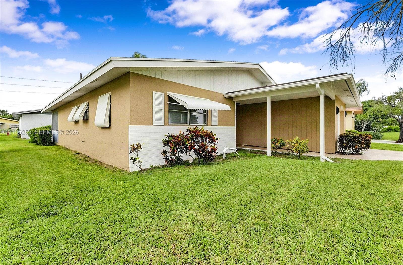 6118 Dusenburg Road, Delray Beach, FL 33484 Single-story exterior featuring a painted stucco and brick facade, covered carport, metal window awnings, and low-maintenance landscaping