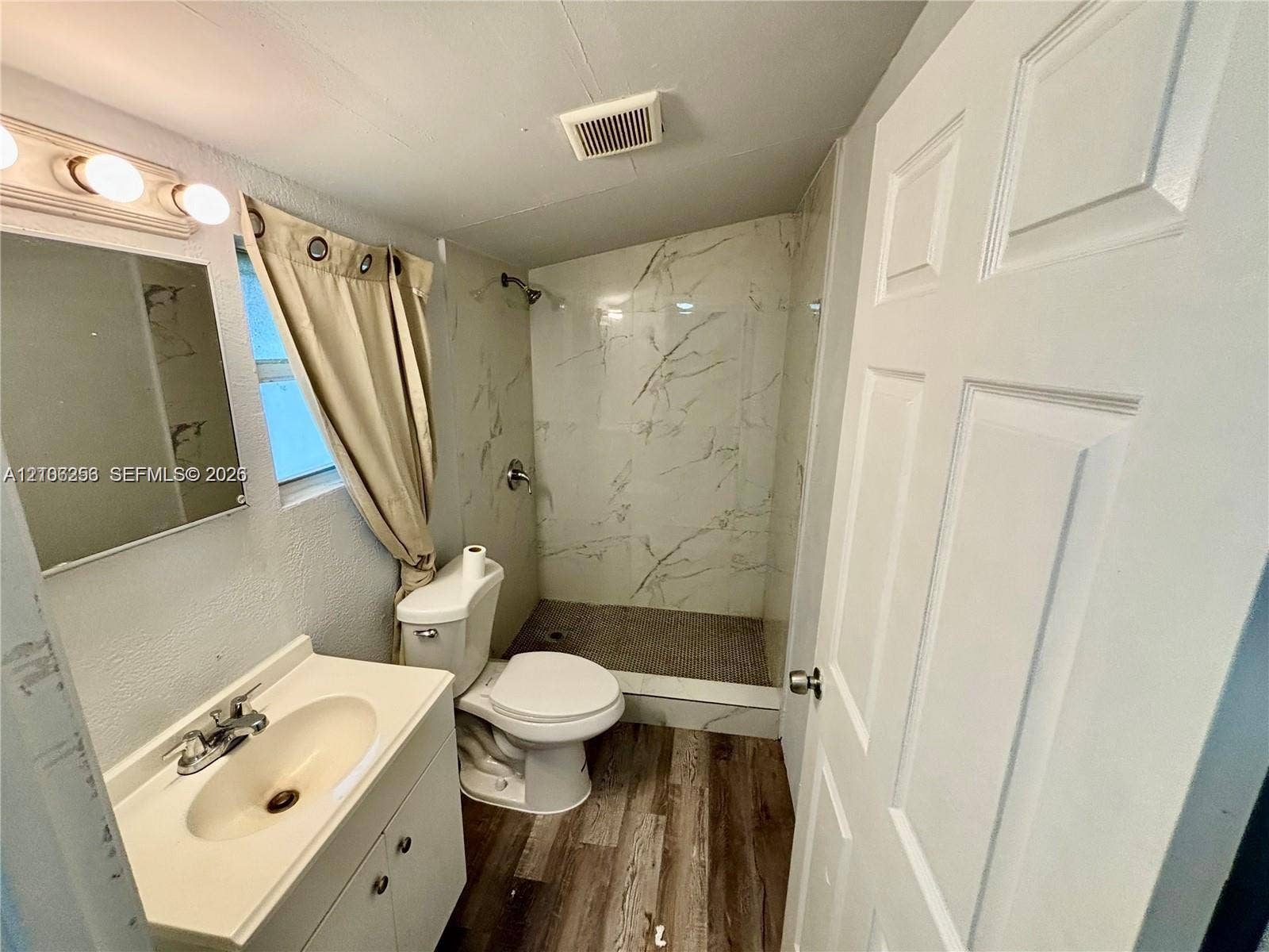 820 21st Street, West Palm Beach, FL 33407 Bathroom featuring wood-finish flooring, a white vanity with an integrated sink, and a walk-in shower with stone-patterned wall tile and a pebble-texture floor