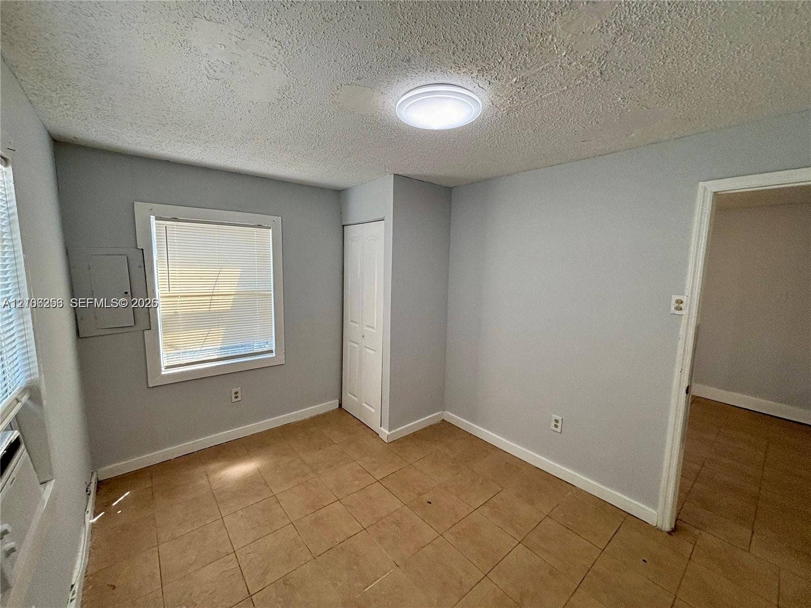 820 21st Street, West Palm Beach, FL 33407 Neutral-toned interior space featuring light-colored tile flooring, flush-mount ceiling lighting, a white panel closet door, and a multi-pane window