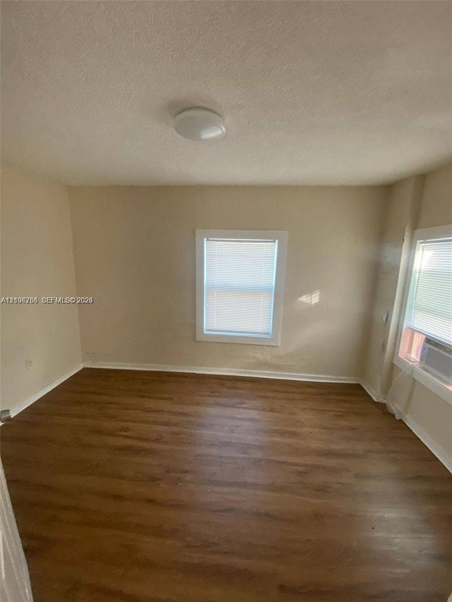 820 21st Street, West Palm Beach, FL 33407 Room featuring wood-finish flooring, neutral-tone walls, two windows with blinds, and a ceiling-mounted light fixture