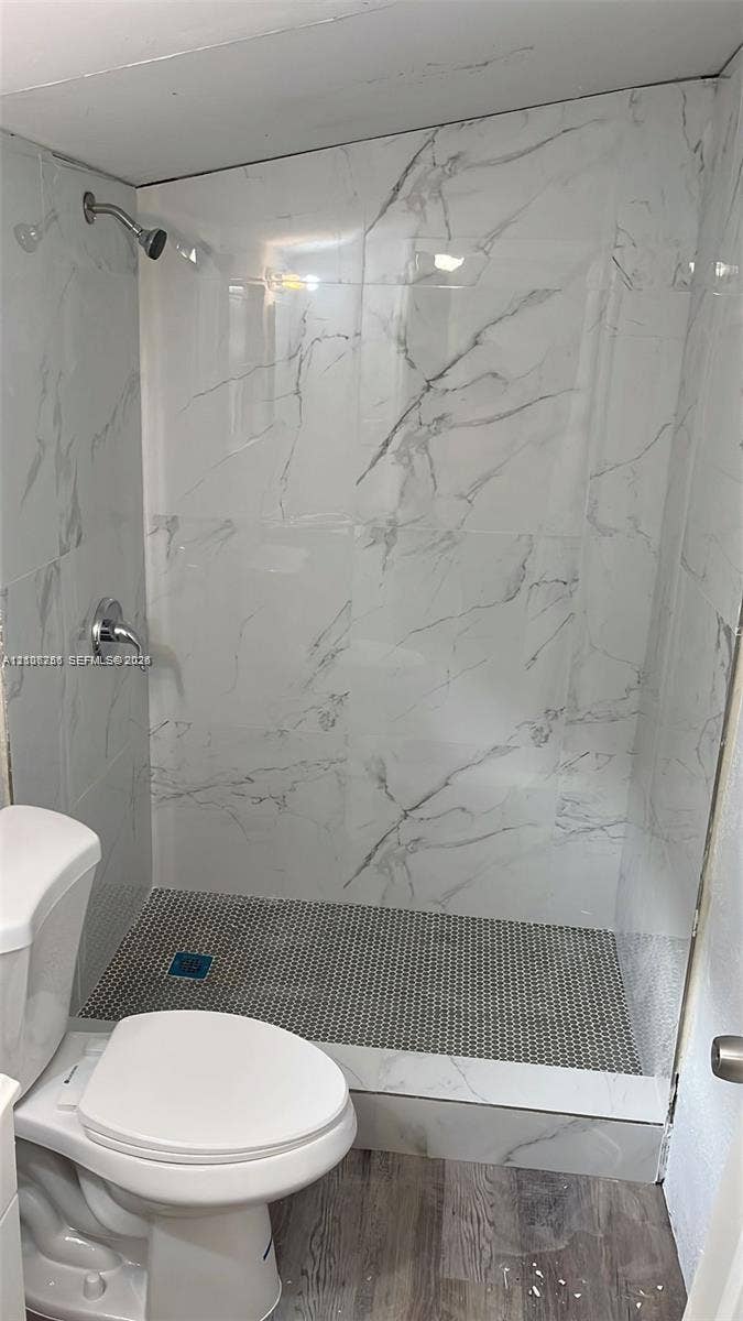 820 21st Street, West Palm Beach, FL 33407 Walk-in shower enclosure featuring large-format white veined wall tile, mosaic-style floor tiling, wall-mounted shower head, and wood-finish flooring
