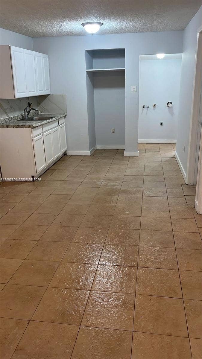 820 21st Street, West Palm Beach, FL 33407 Utility area featuring ceramic tile flooring, white cabinetry with speckled stone-finish countertops, stainless steel sink, and dedicated appliance alcove