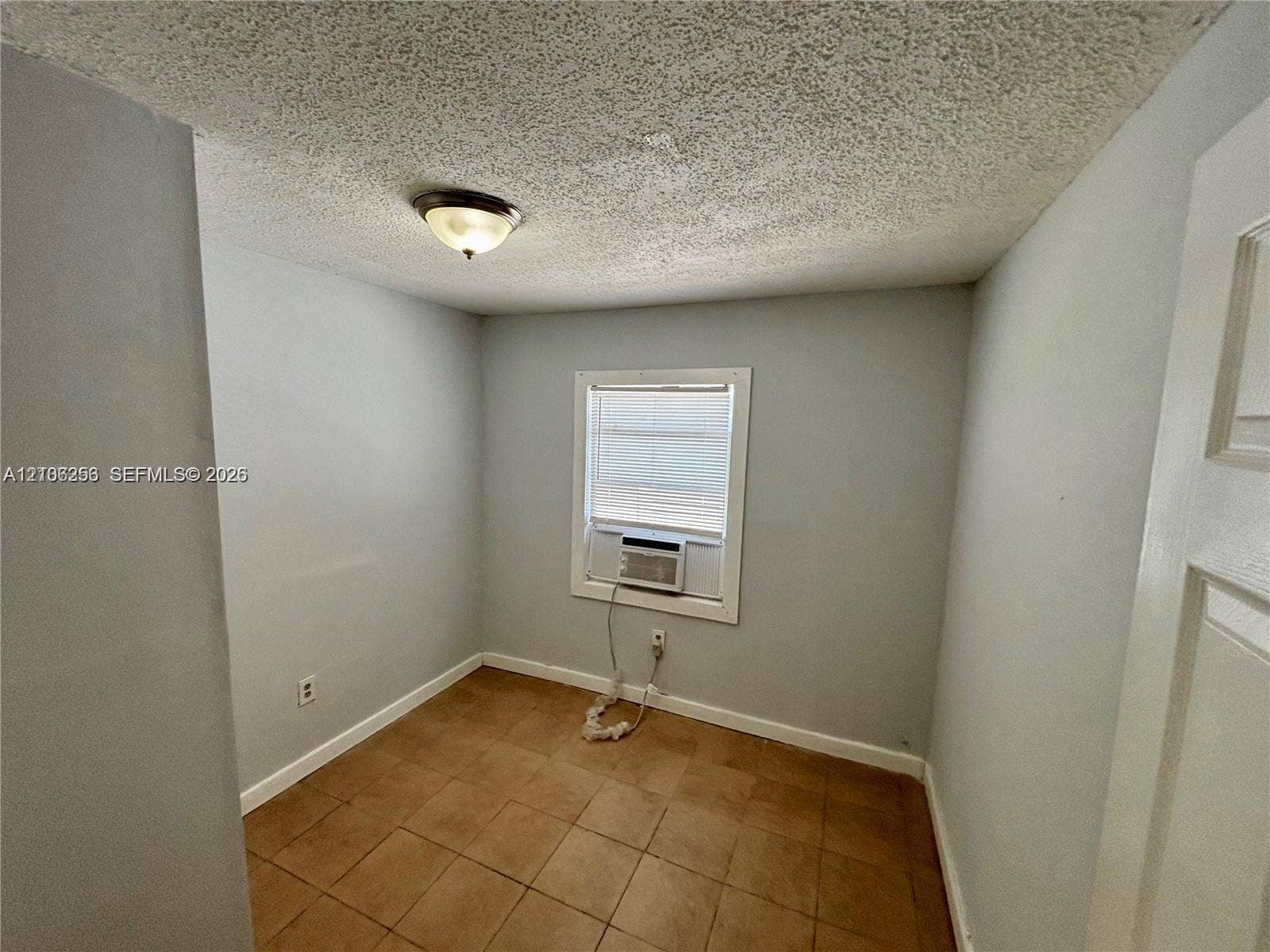820 21st Street, West Palm Beach, FL 33407 Room featuring tile flooring, textured ceiling, flush-mount lighting, and a single-hung window with an integrated air conditioning unit